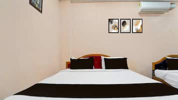 A hotel room with a bed, a wall-mounted air conditioner, and three framed artworks.
