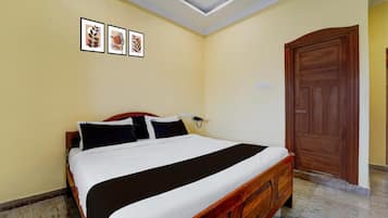 A hotel room with a single bed, a wooden wardrobe, a wall-mounted telephone, and three framed pictures.