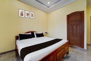 A hotel room with a single bed, a wooden wardrobe, a wall-mounted telephone, and three framed pictures. - Deluxe kk Residency (Karaikal)