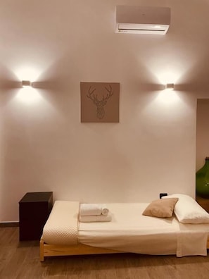 A single bed with a headboard, a wall-mounted air conditioner, and two wall-mounted lights. - L angolo delle bugie (TURI)