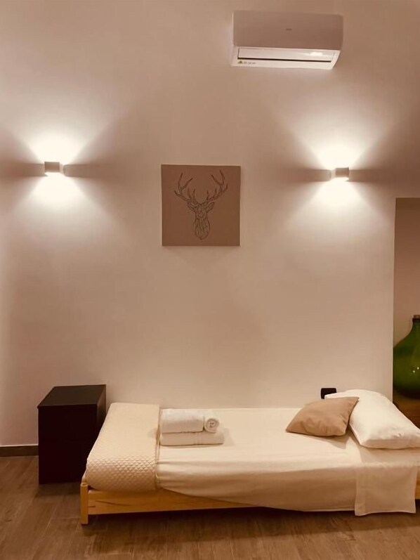 A single bed with a headboard, a wall-mounted air conditioner, and two wall-mounted lights.