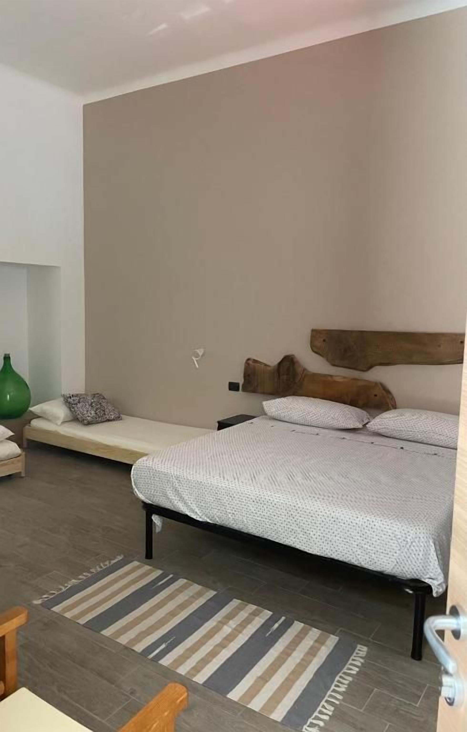 Un dormitorio con una cama, un banco, un jarrón verde y una alfombra a rayas.