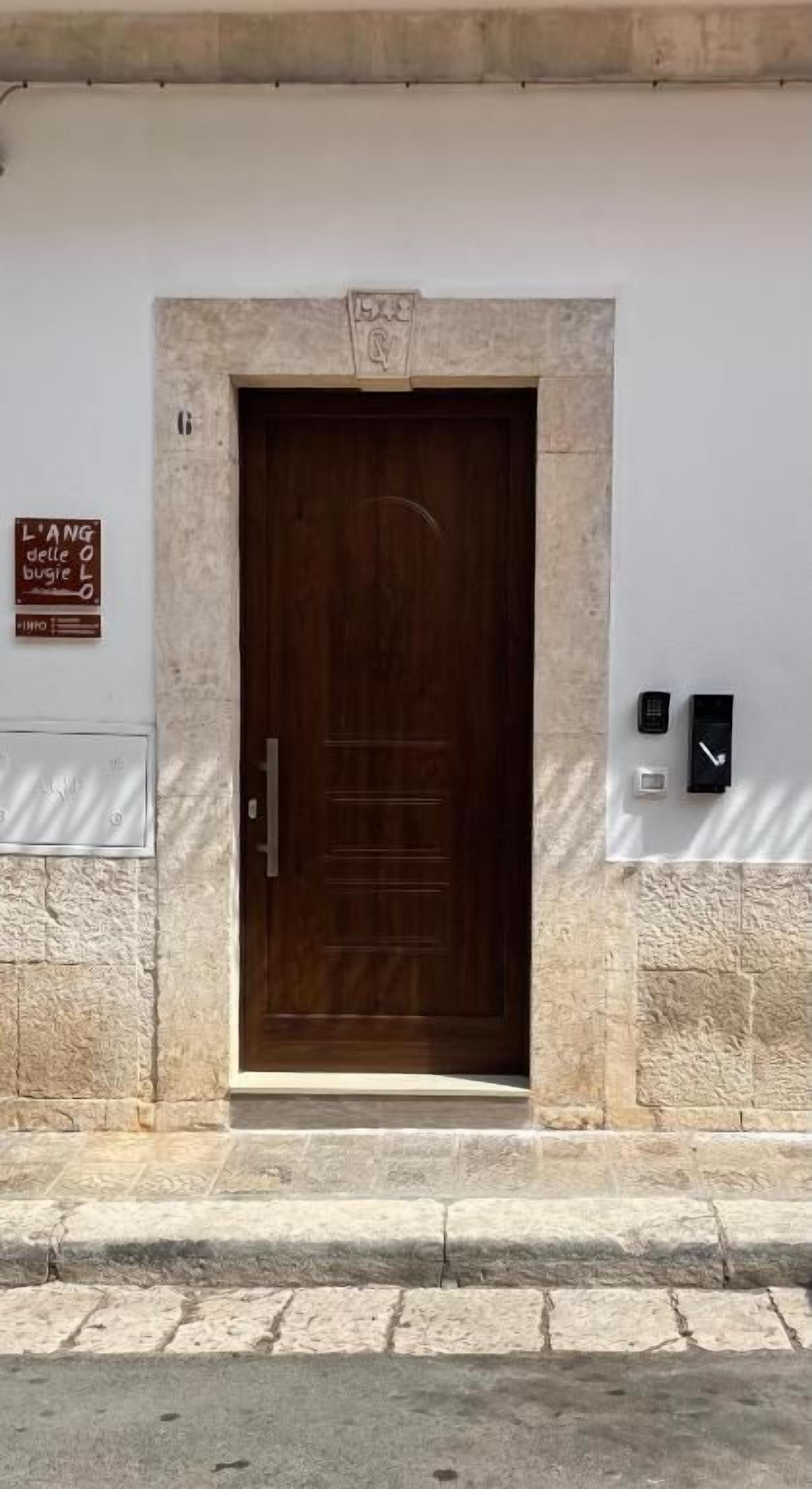 Une porte en bois encadrée de pierre, une enseigne au-dessus, et deux appareils fixés au mur sur le côté droit.