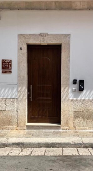 A wooden door with a stone frame, a sign above it, and two wall-mounted devices to the right.