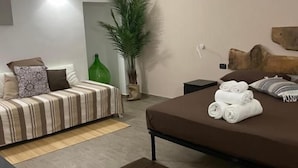 Ein modernes Schlafzimmer mit einem Bett, einem Schlafsofa, einem Nachttisch und einer Topfpflanze.