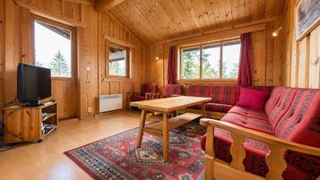 Een houten cabin met een bank, tafel en televisie.