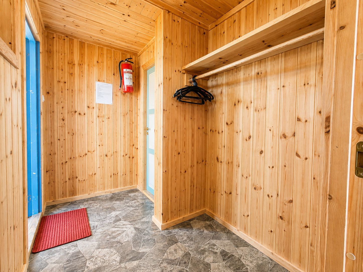 Un intérieur en bois, avec un extincteur, un tapis rouge et un porte-manteau.