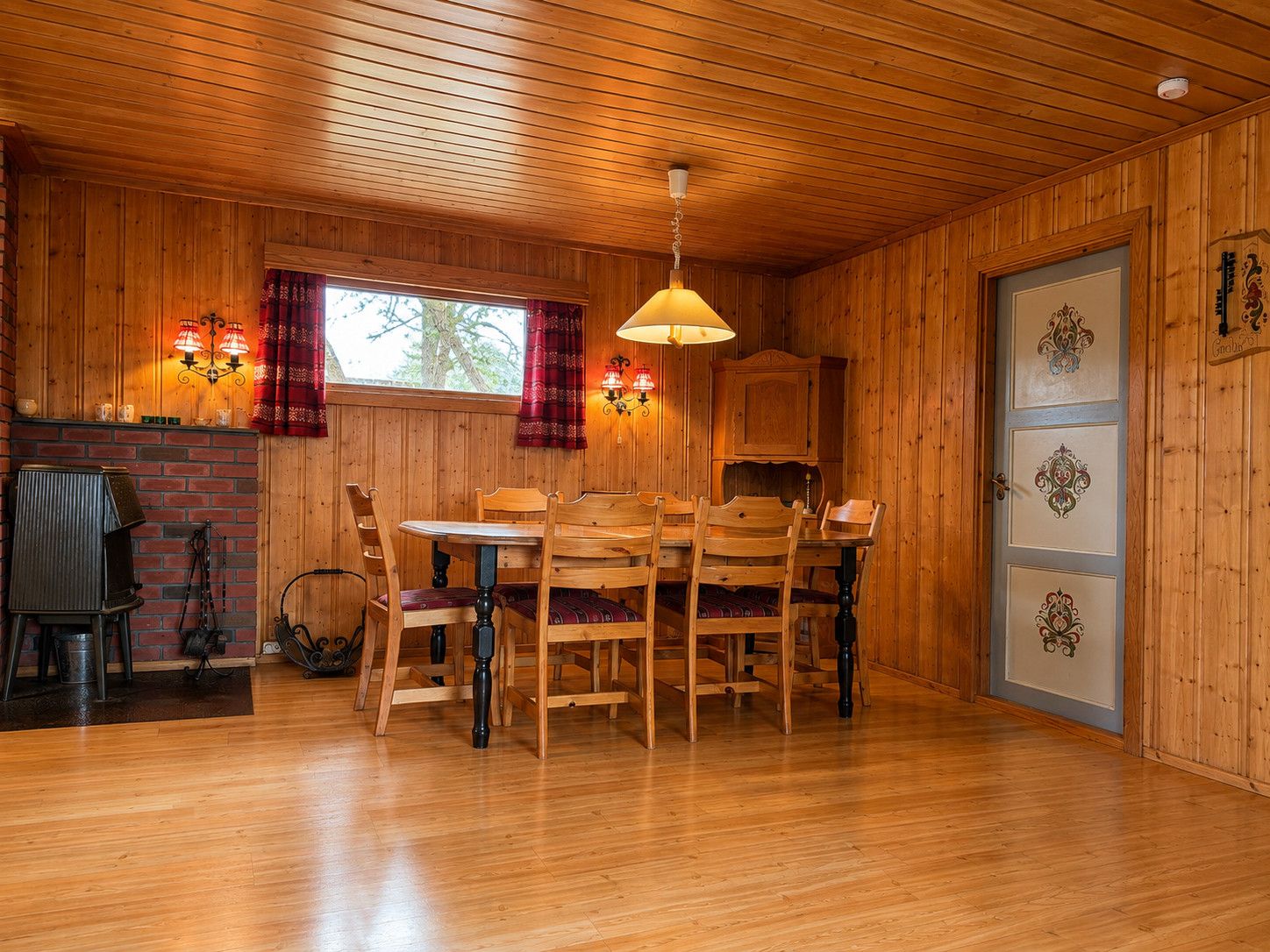 A wooden interior with a dining table and chairs, a brick wall, and a window with curtains.