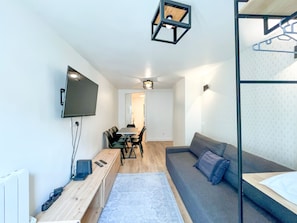 A modern, compact living space with a sofa, a dining table with chairs, a TV mounted on the wall, and a small wooden desk with a computer and remote controls. - 152 - Urban Cosy Flat in Paris (París)