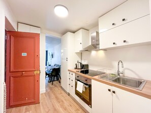 Eine kleine Küche mit weißen Schränken, einer Edelstahl-Spüle und einer Holzausziehtafel.