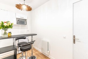 A modern kitchen with a microwave, a bar stool, a vase with flowers, and a unique ceiling light fixture. - 147 - Urban Cosy Flat in Paris (París)