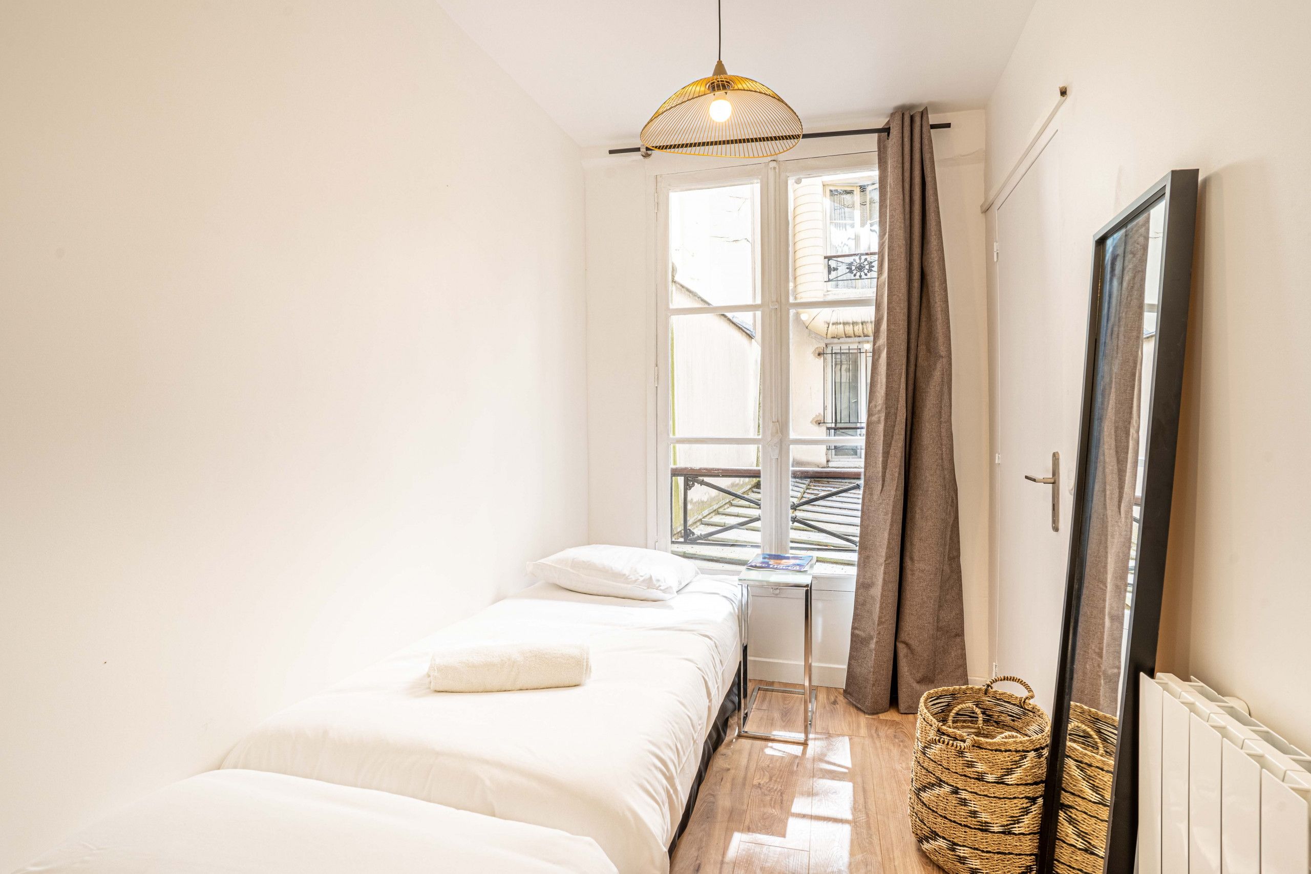 A bedroom with a bed, a window, a radiator, and a woven basket.