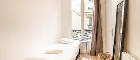 A bedroom with a bed, a window, a radiator, and a woven basket.