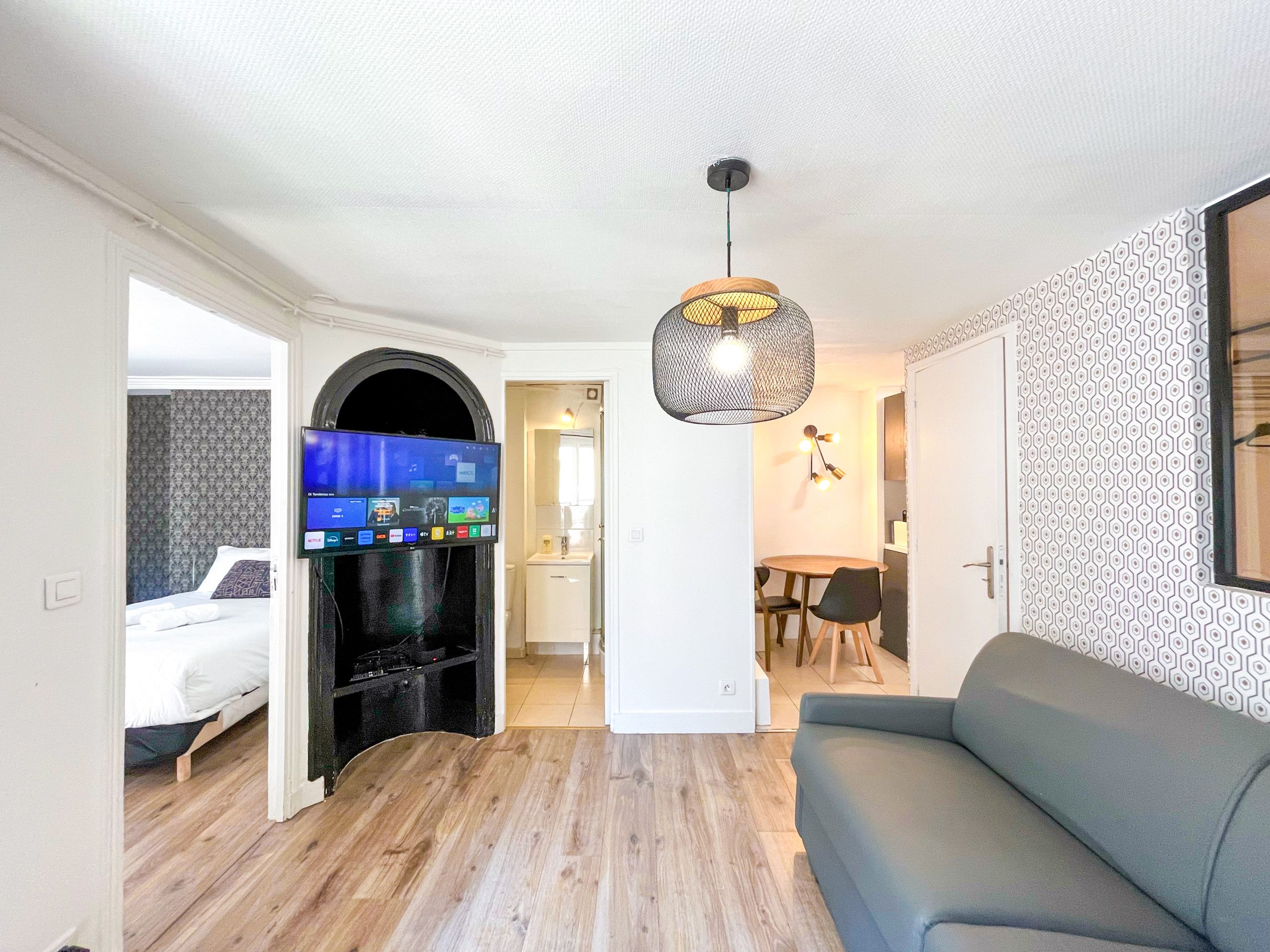 Ein modernes Wohnzimmer mit einer Couch, einem an der Wand montierten Fernseher und einem Essbereich mit Tisch und Stühlen.