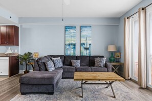 Un salon avec un canapé d’angle, une table basse et une grande fenêtre avec des rideaux.