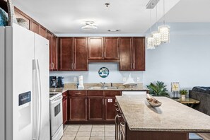 Eine moderne Küche mit Holzausstattung, einem weißen Kühlschrank, einem Einbauofen, einer Arbeitsplatte aus Granit und einer Pendelleuchte.