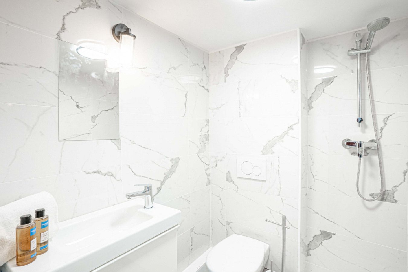 A bathroom with a white marble sink, a toilet, and a shower with a handheld showerhead.