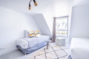 A modern bedroom with a bed, bedside table, and a view of buildings through a window. - 145 - Urban Pretty Studio in Center of Paris (París)
