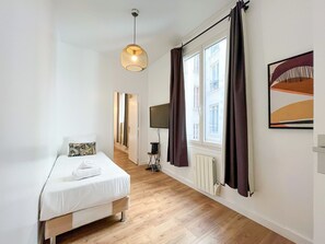 A hotel room with a bed, a television, a radiator, and a window with curtains. - 146 - Urban Cosy Flat in Paris (París)