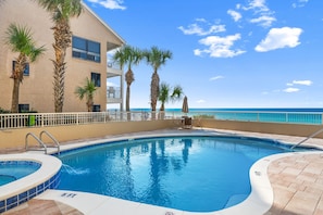 A swimming pool with a view of the ocean, surrounded by palm trees and a building with balconies. - Spacious Coastal Retreat | Complimentary Beach Service (Destin)
