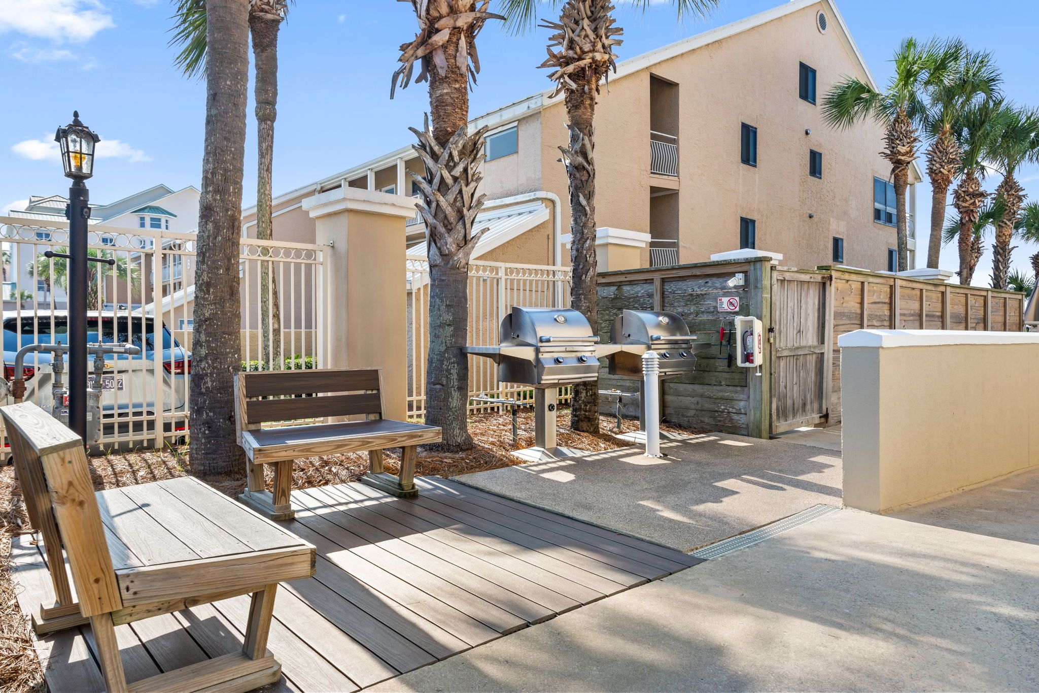 An outdoor patio area with a wooden bench, a grill, and a wooden fence.