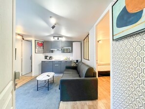 A modern living room with a sectional sofa, a coffee table, and a kitchen area with grey cabinets and a microwave. - Urban Flat 150 - Pretty Flat in Center of Paris (París)