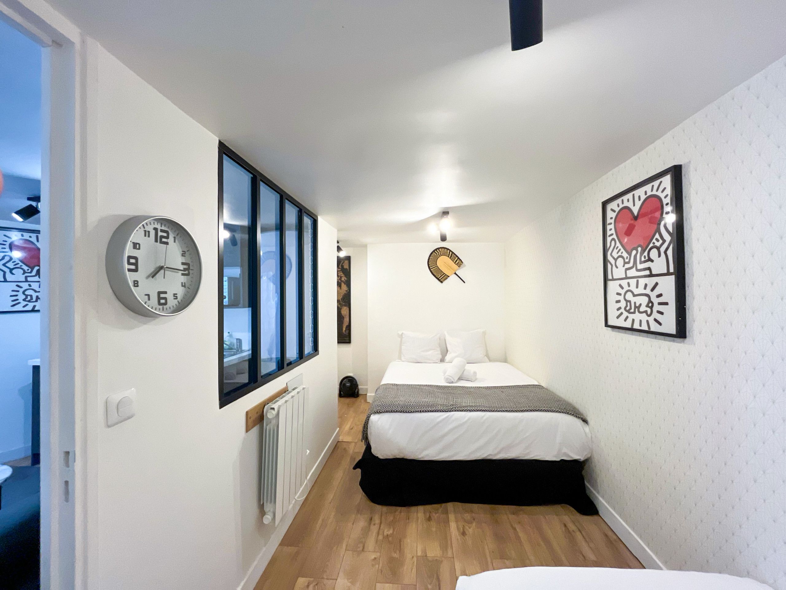 A hotel room with a bed, a clock, a radiator, and a window.