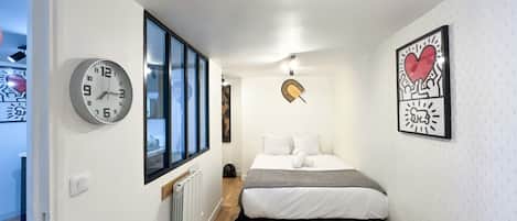 A hotel room with a bed, a clock, a radiator, and a window.