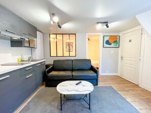 A compact living space with a kitchenette, a sofa, a coffee table, and a door leading to another room. - Urban Flat 150 - Pretty Flat in Center of Paris (París)