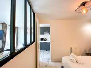 A hotel room with a bed, a window with curtains, a kitchen area visible through an open door, and a unique light fixture. - 143 - Urban Charming Flat in Center of Paris (París)