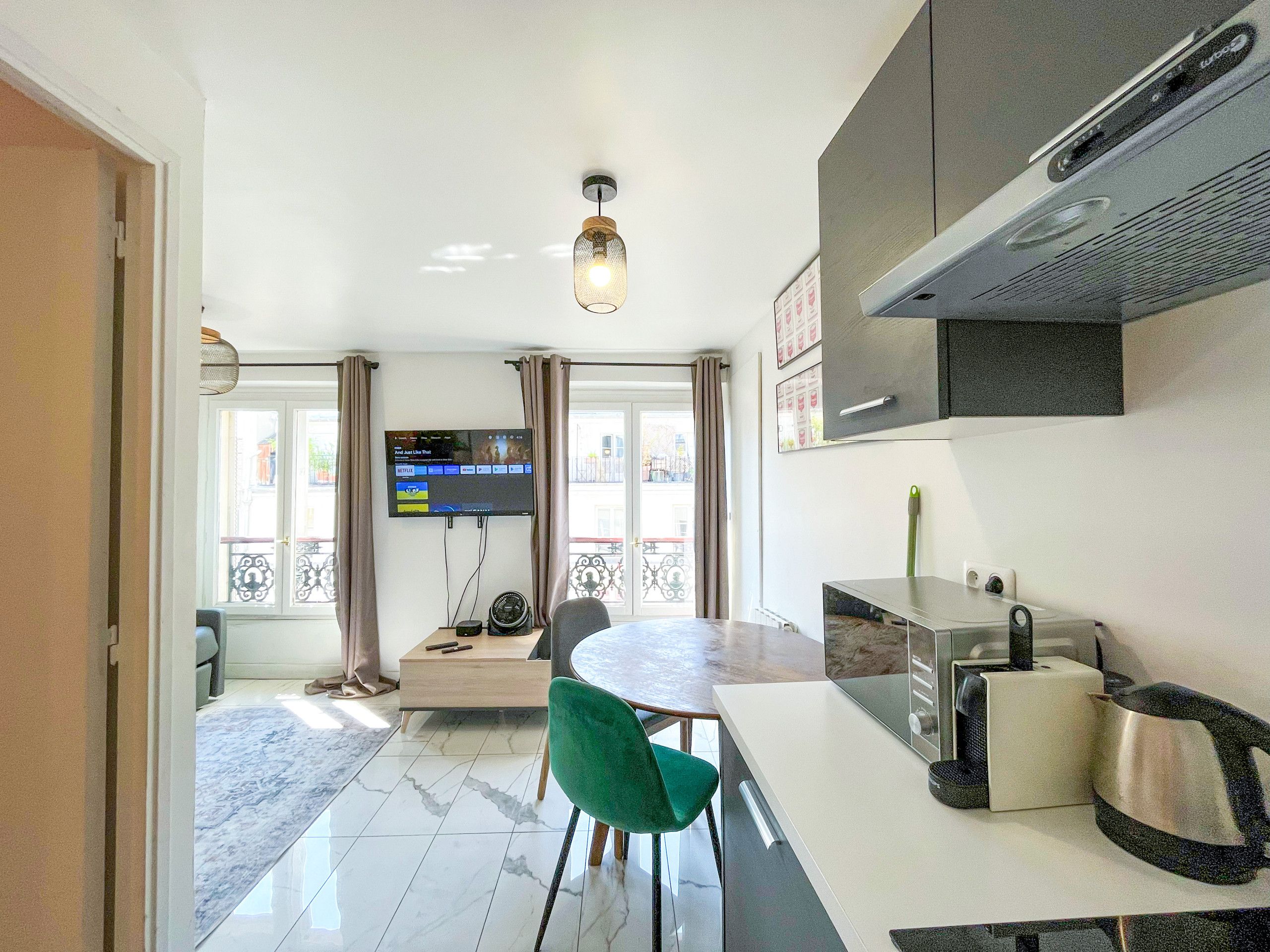 A modern kitchen with a flat-screen TV, a dining table with chairs, and a coffee machine.