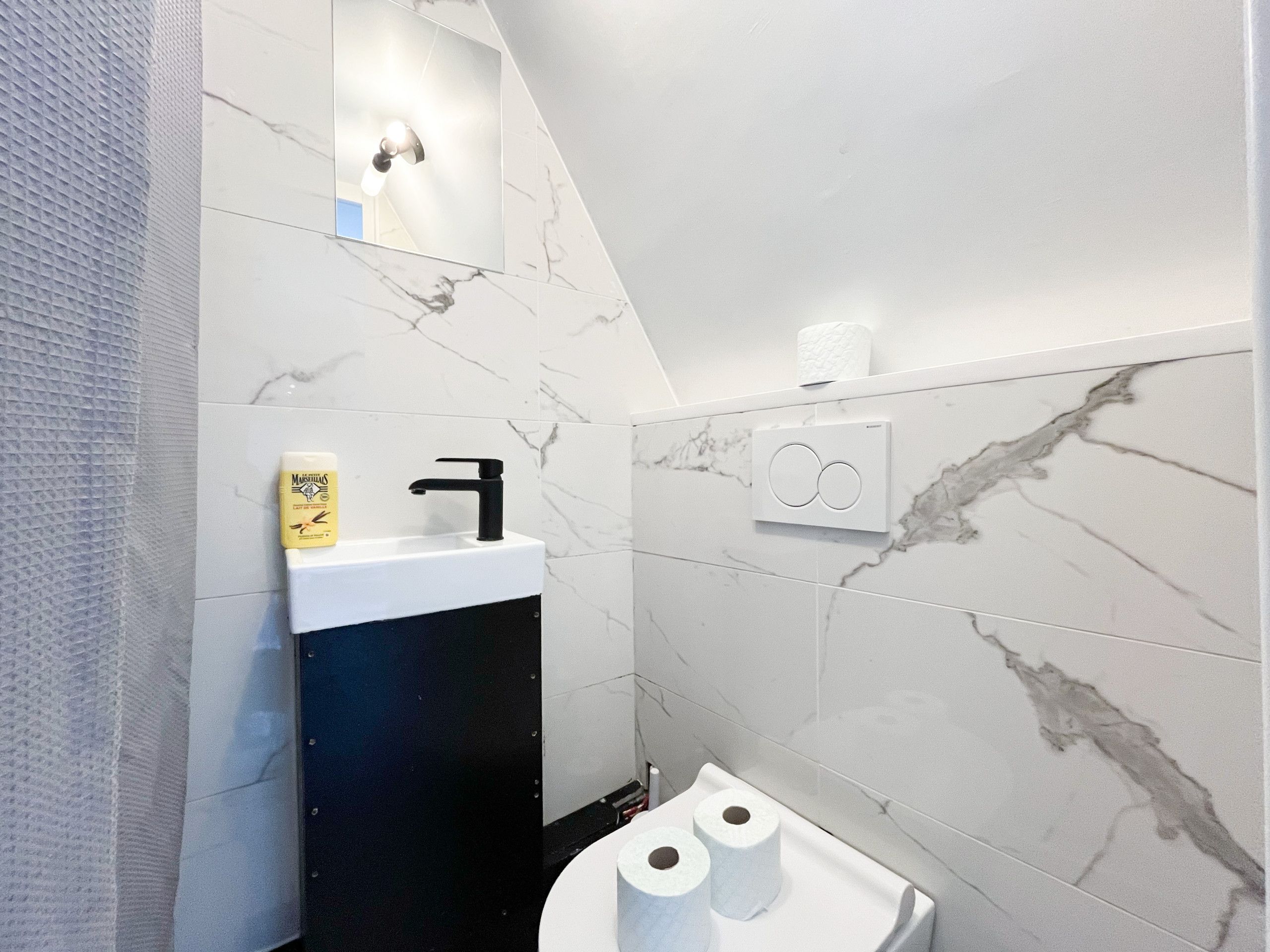 Ein Badezimmer mit einem weißen Waschbecken, einem schwarzen Wasserhahn und Marmorwänden.