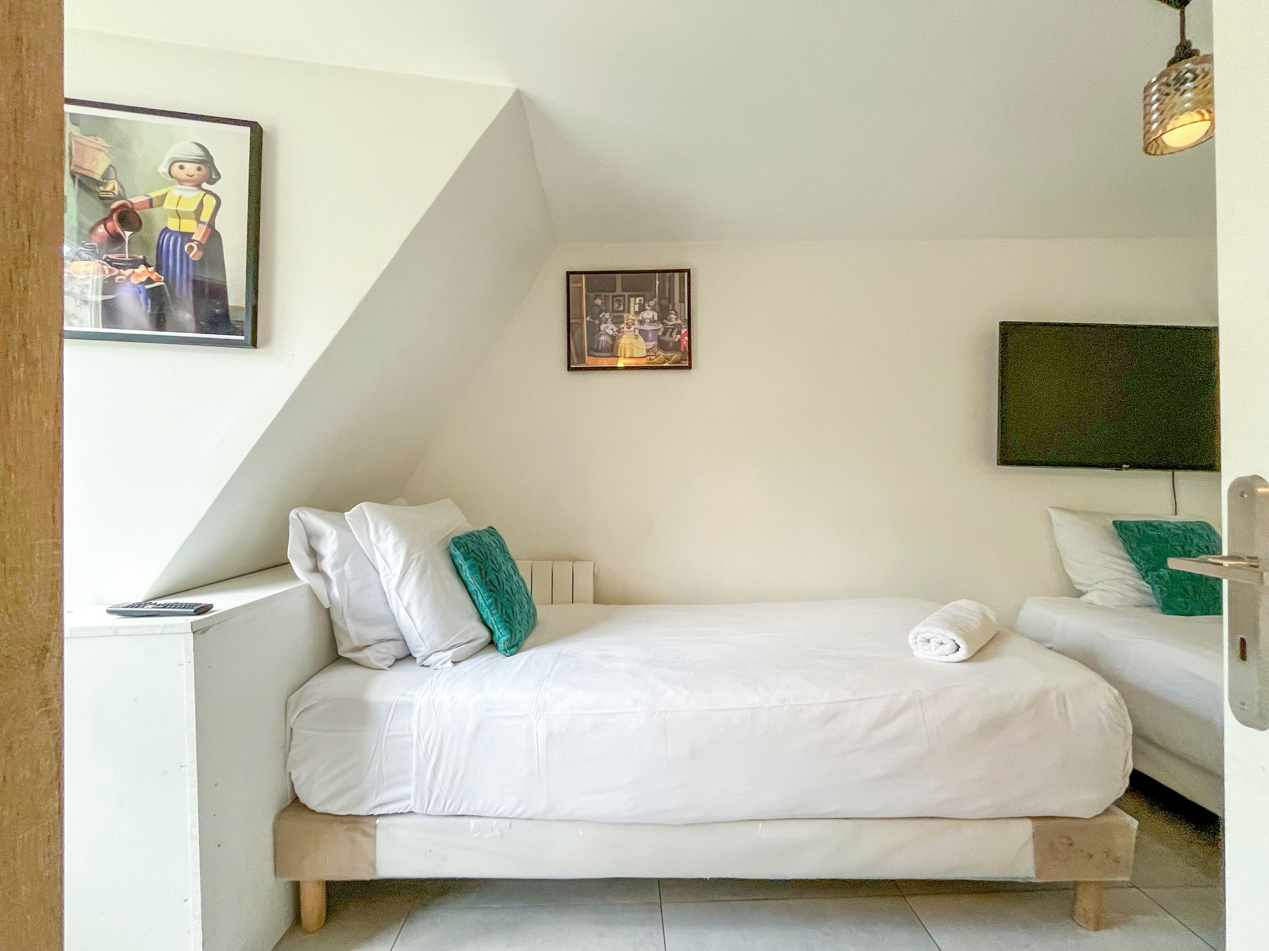 Une chambre à coucher avec un lit, des oreillers, une table de chevet, un téléviseur et un tableau accroché au mur.