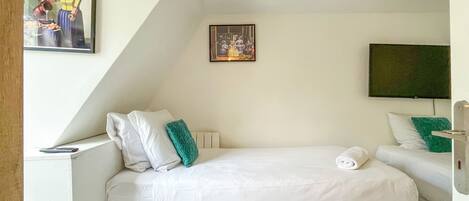 Une chambre à coucher avec un lit, des oreillers, une table de chevet, un téléviseur et un tableau accroché au mur.