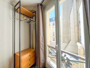 A small room with a wooden bench, a metal rack with hangers, and a window with a view of buildings. - 142 - Urban Pretty Flat in Montorgueil (París)