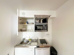 Een kleine keuken met een spoelbak, fornuis, magnetron en planken voor opslag.