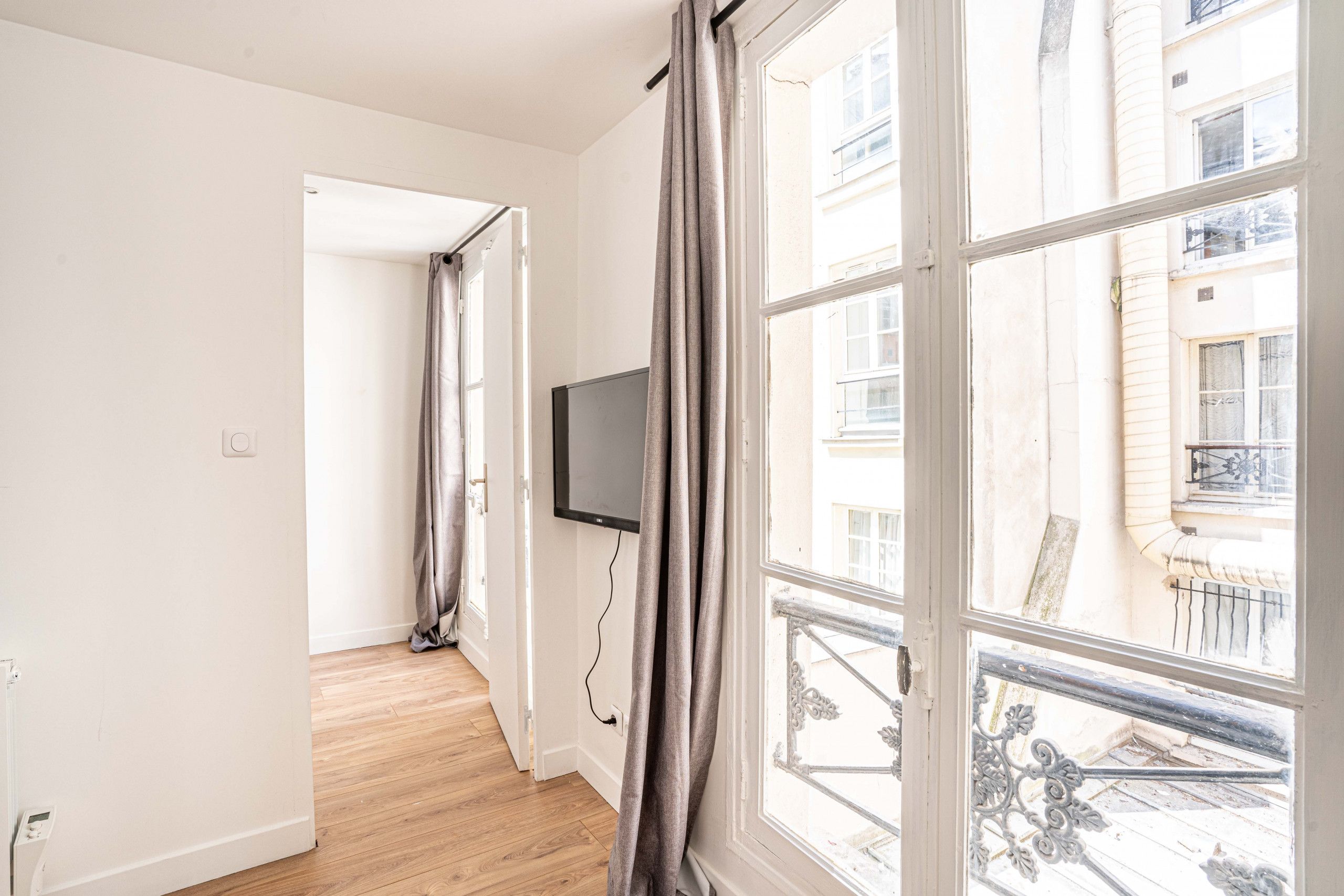 A corridor with a television mounted on the wall, leading to an open door.