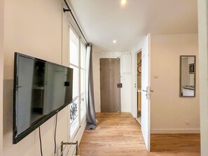 Ein Flur mit einem an der Wand befestigten Fernseher, einer Tür am Ende und einem Spiegel.