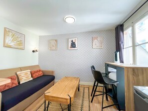 A furnished living space with a sofa, a wooden table, a chair, a patterned wall, and a window. - 163 - Urban Studio in Paris (París)