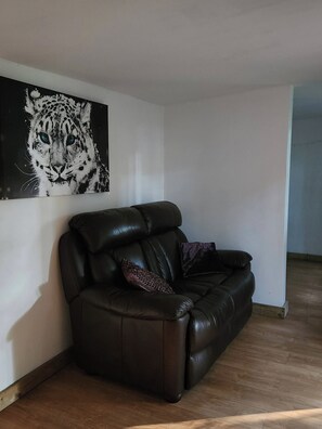 A dark leather sofa with a single decorative pillow against a white wall, with a large black and white artwork above it. - Badgers Den at The Secret Garden (Ashford)