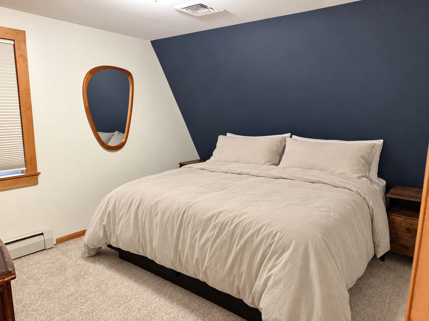 Une chambre à coucher comprenant un lit, une table de chevet, un miroir à cadre en bois et un radiateur fixé au mur.