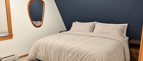 Ein Schlafzimmer mit einem Bett, einem Nachttisch, einem spiegelnden Holzrahmen und einem Wandheizkörper.