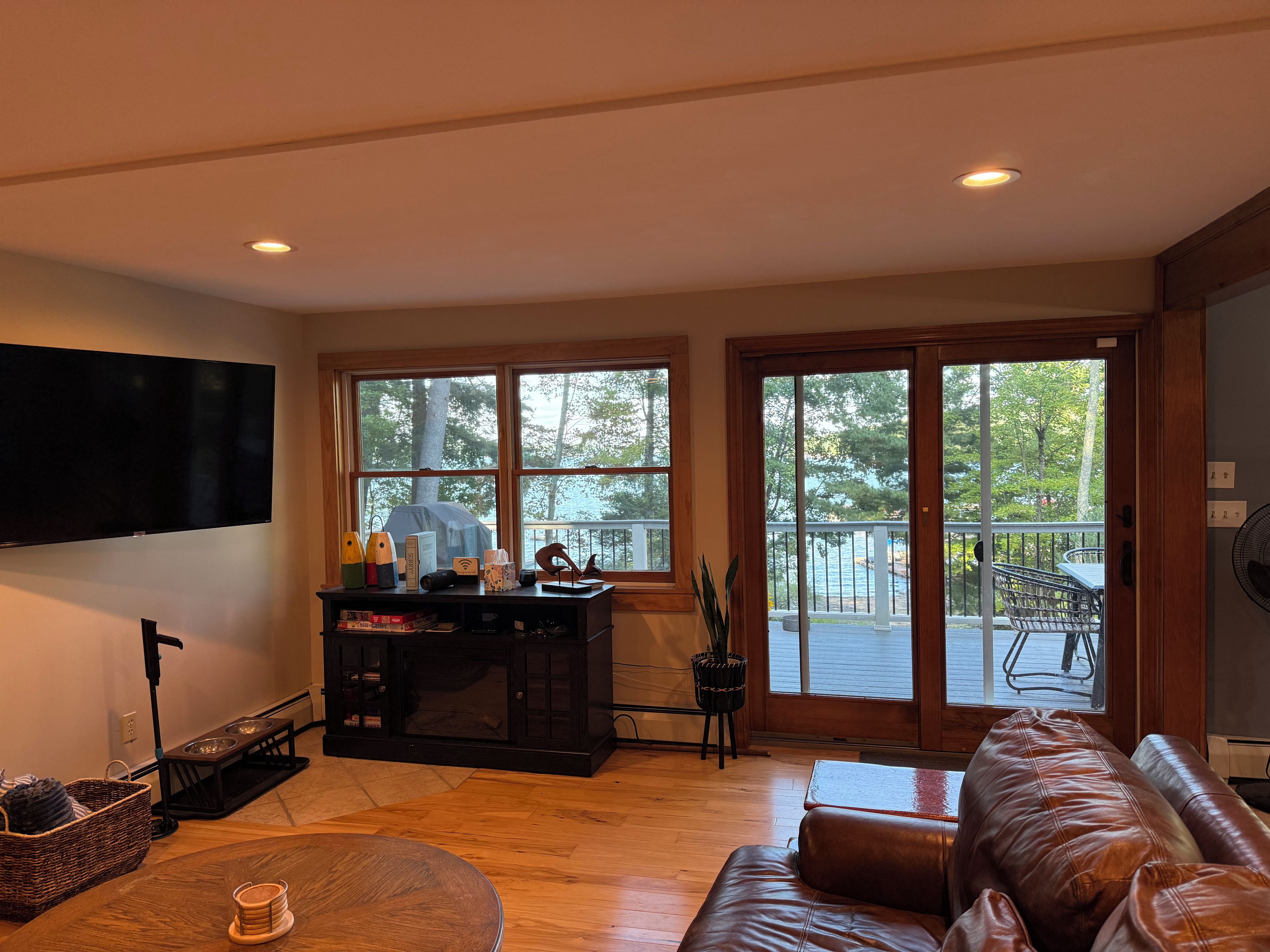 Una sala de estar con un sofá de cuero, un televisor montado en la pared, una mesa de centro de madera y un ventanal con vistas al exterior.