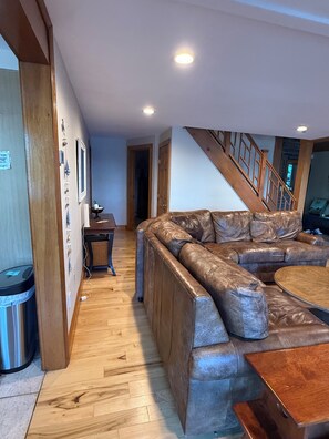 Ein Wohnzimmer mit einem ledernen Ecksofa, einem Holztisch und einer Treppe, die nach oben führt.