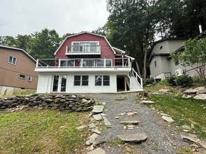 A two-story house with a balcony, a stone wall in front, and a gravel path leading to the entrance. - Waterfront house on Lake Wallenpaupack w/ private dock, sleeps 9, dogs allowed! (Tafton)