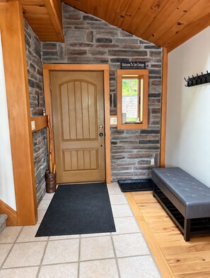 A wooden door with a black mat, a bench, and a stone wall. - Waterfront house on Lake Wallenpaupack w/ private dock, sleeps 9, dogs allowed! (Tafton)