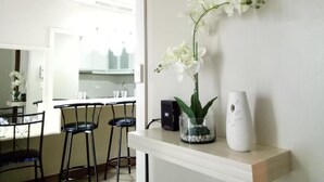 A modern kitchen with white cabinets, a bar area with stools, and a white orchid in a glass vase on the counter. - Kim's hub at Two Palmtree Villas (Pasay City)