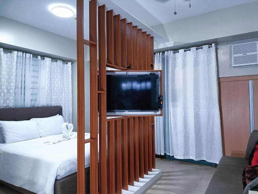 A hotel room with a bed, a TV mounted on a wooden panel, and a window with curtains.