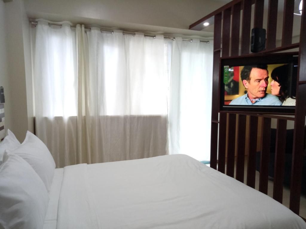 A hotel room with a bed, curtains, a television, and a wall-mounted TV.