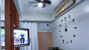 A living room with a television, a clock on the wall, a ceiling fan, and a sofa with cushions. - Kim's hub at Two Palmtree Villas (Pasay City)